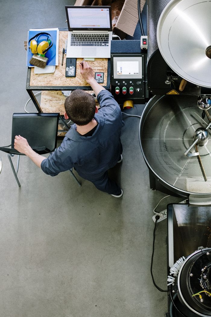 services-04 Overhead view of technician operating coffee roasting equipment in an industrial setting.